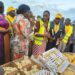 Hajjati Namyalo Centre with a Microphone delivers chicken and chicken feeds to the people of Bukomansimbi